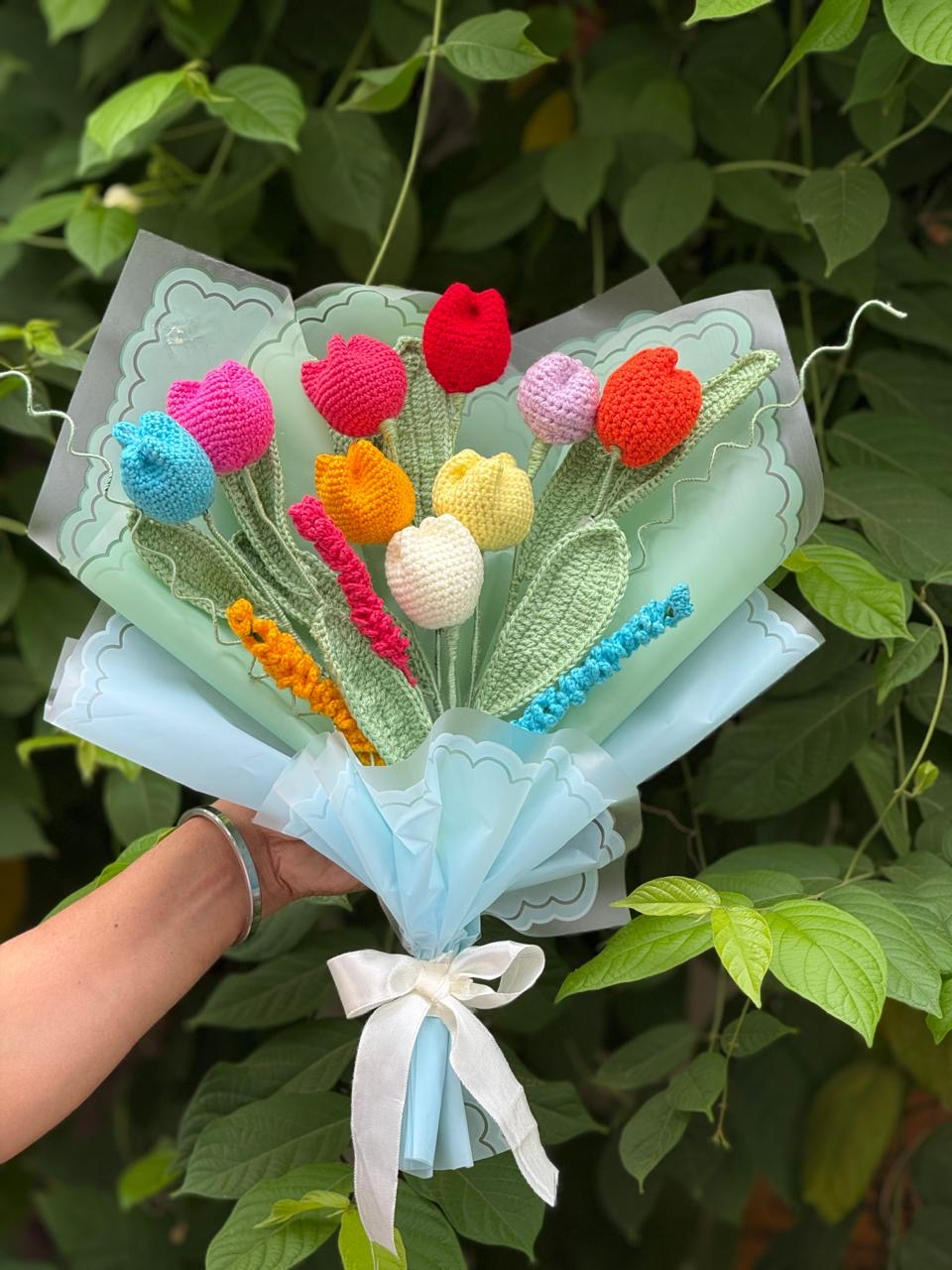 Bouquet of brightly colored handmade crochet tulips wrapped in mint paper, held up in a garden